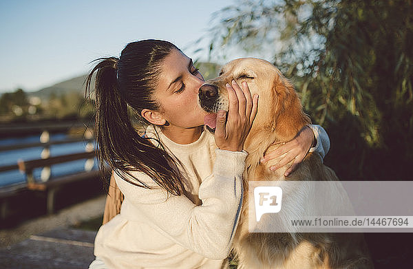 Junge Frau küsst ihren Golden-Retriever-Hund am Wasser