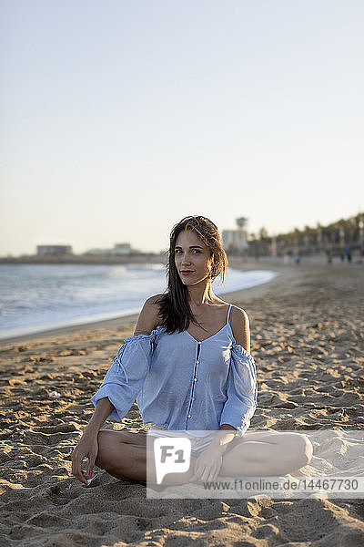 Porträt einer schönen Frau am Strand  die im Schneidersitz im Sand sitzt