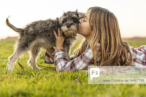 Mädchen liegt auf einer Wiese und küsst ihren Hund