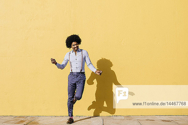 Lächelnder Mann tanzt vor der gelben Wand