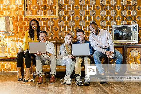 Gruppe von lächelnden Menschen  die auf einer Couch im alten Wohnzimmer mit Laptops sitzen