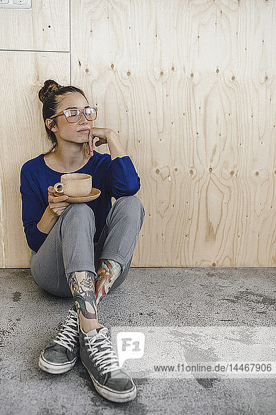 Junge Frau macht eine Pause im Büro und trinkt Kaffee aus einer Holztasse
