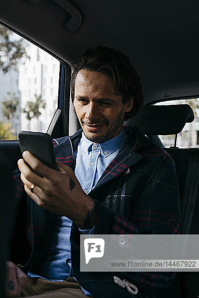 Lächelnder Mann sitzt auf dem Rücksitz eines Autos und benutzt ein Mobiltelefon