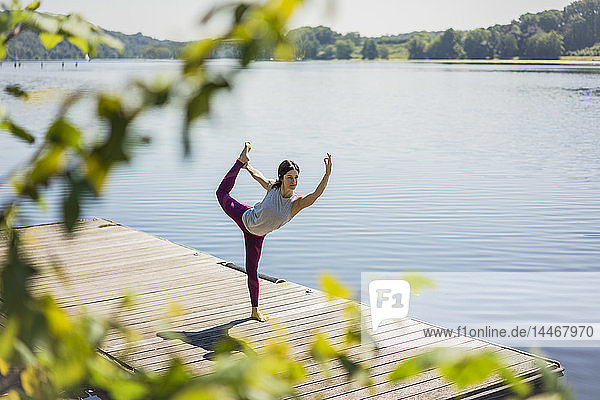 Reife Frau  die im Sommer auf einem Steg an einem See Yoga praktiziert