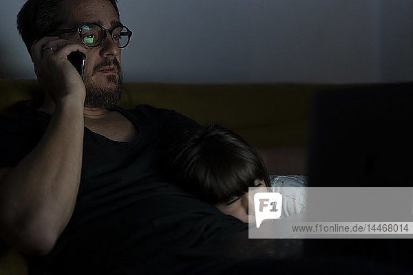 Father talking on cell phone on couch at night with daughter sleeping