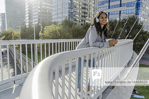 Junge Frau steht auf einer Brücke  hört Musik  benutzt ein Smartphone