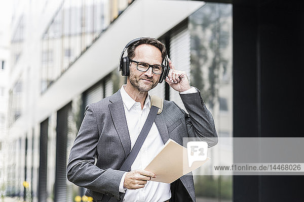 Porträt eines lächelnden Geschäftsmannes mit Dokumenten und Kopfhörern