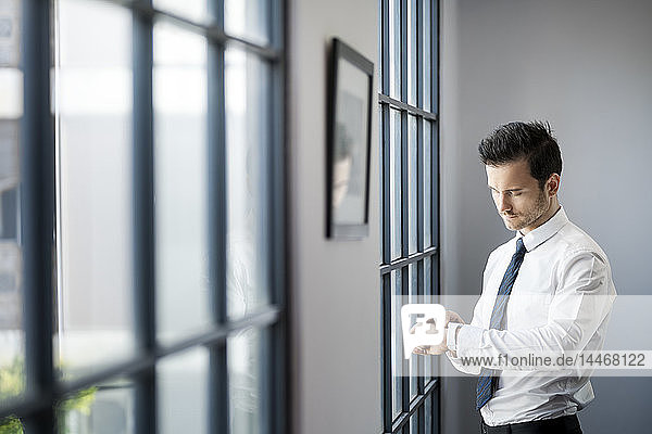 Businessman checking smartwatch in front of large office window