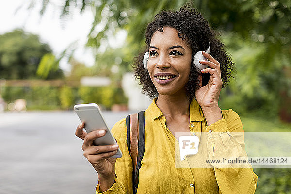 Porträt einer lächelnden Frau  die im Freien mit Kopfhörern und Smartphone Musik hört