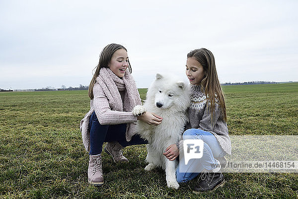 Zwei Mädchen kauern auf einer Wiese und unterrichtenden Hund