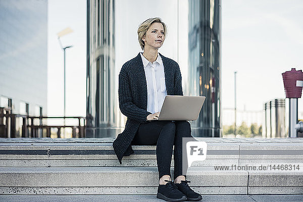 Junge Geschäftsfrau sitzt auf einer Treppe und benutzt einen Laptop