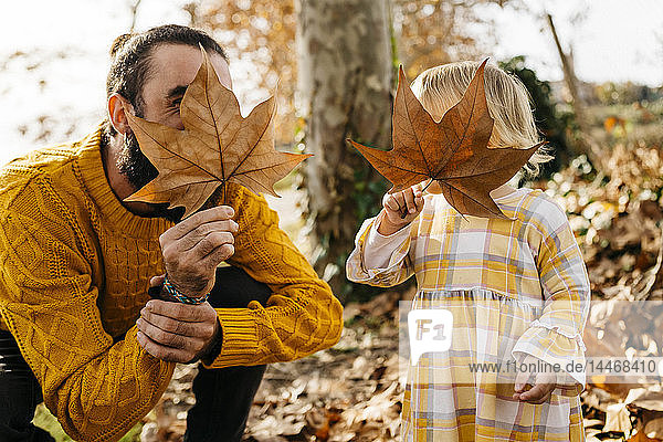 Vater und Tochter genießen im Herbst einen Vormittag im Park und spielen mit Herbstblättern