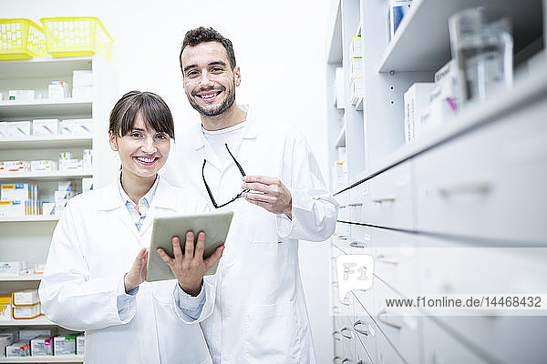 Portrait of two smiling pharmacists with tablet in pharmacy