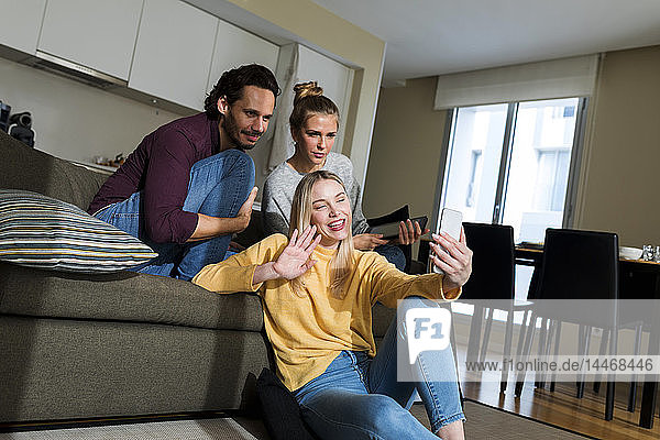 Freunde sitzen auf der Couch im Wohnzimmer  nutzen das Smartphone  plaudern