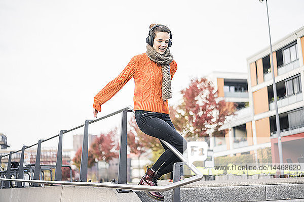 Porträt einer lachenden Frau mit schnurlosen Kopfhörern  die ein Geländer herunterrutscht