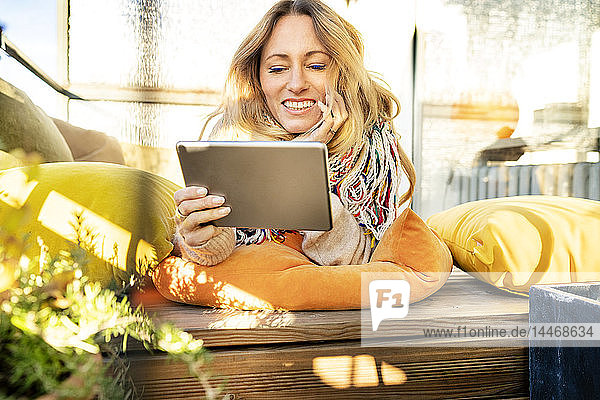 Porträt einer lächelnden  blonden  reifen Frau  die sich im Wintergarten mit einem digitalen Tablet entspannt