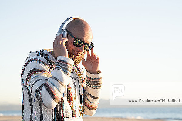 Mann mit Kopfhörer und Sonnenbrille am Strand