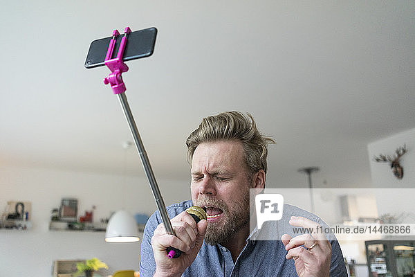 Mann singt zu Hause in ein Mikrofon  das an einem Selfie-Stock befestigt ist
