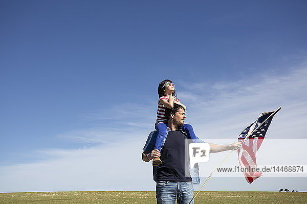 Man with daughter and American flag on field in remote landscape