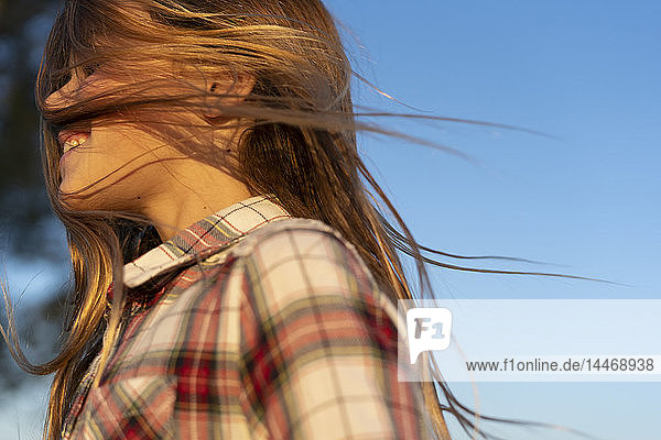 Profil eines lachenden Mädchens mit wehendem Haar vor blauem Himmel