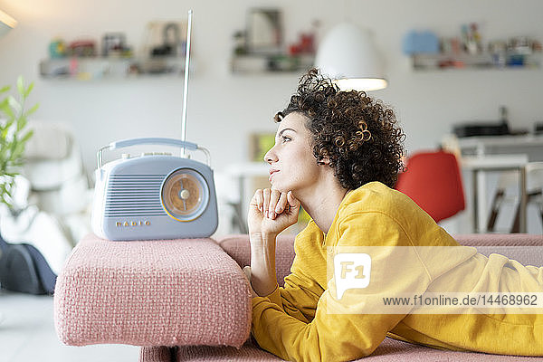 Frau liegt auf dem Sofa und hört zu Hause Musik mit einem tragbaren Radio