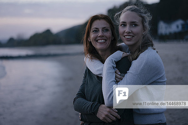 Deutschland  Hamburg  glückliche Mutter und junges Mädchen umarmen sich abends am Strand am Elbufer
