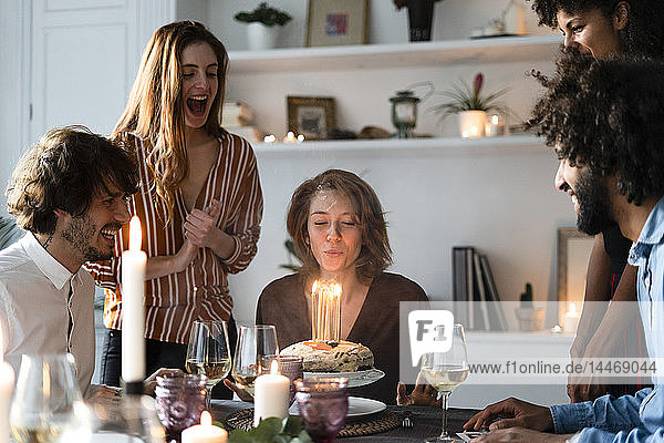 Friends surprising young woman with a birthday cake with burning candles