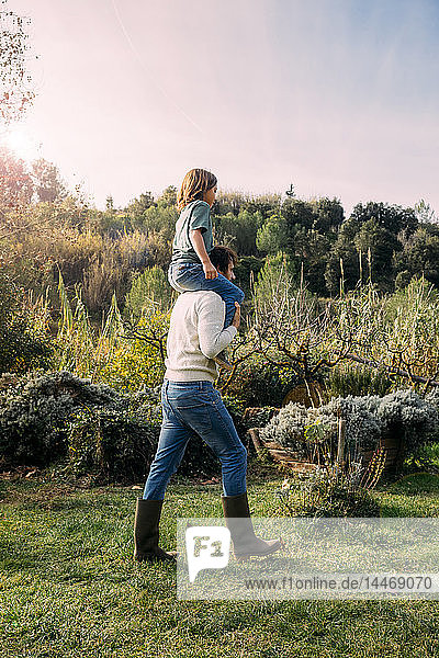 Vater spielt mit seinem Sohn und trägt ihn huckepack in einem Garten