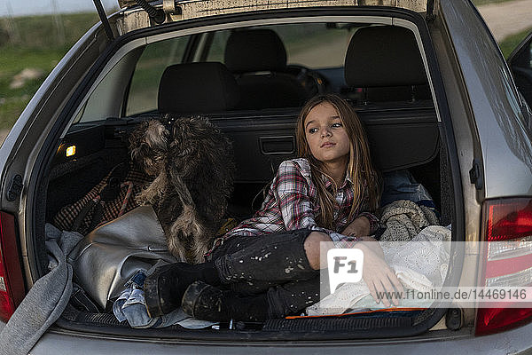 Mädchen wartet abends mit ihrem Hund im geparkten Auto