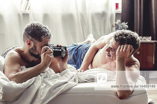 Schwuler Mann fotografiert seinen Partner mit altmodischer Kamera im Bett