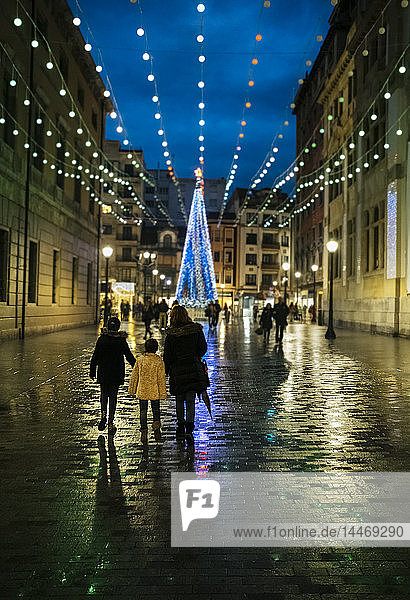 Spanien  Gijon  Rückenansicht von Mutter und zwei Kindern  die abends zur Weihnachtszeit in der Fußgängerzone spazieren gehen
