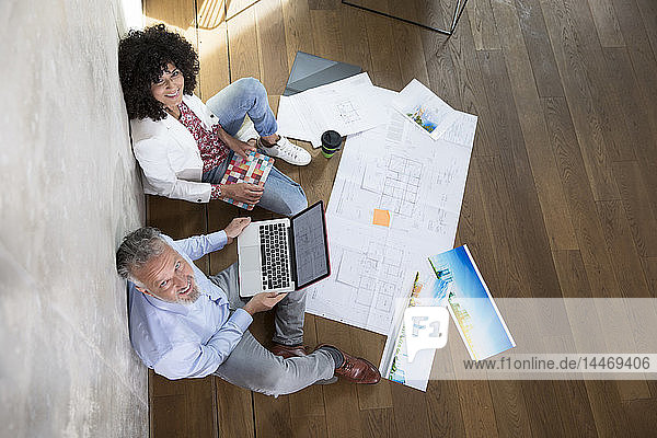 Geschäftsmann und Geschäftsfrau sitzen auf dem Boden in einem Loft und arbeiten mit Laptop und Dokumenten