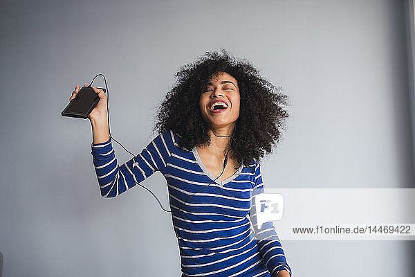 Porträt einer glücklichen jungen Frau mit Smartphone und Kopfhörern beim Singen und Tanzen