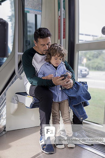 Vater und Sohn telefonieren mit dem Handy in einer Straßenbahn