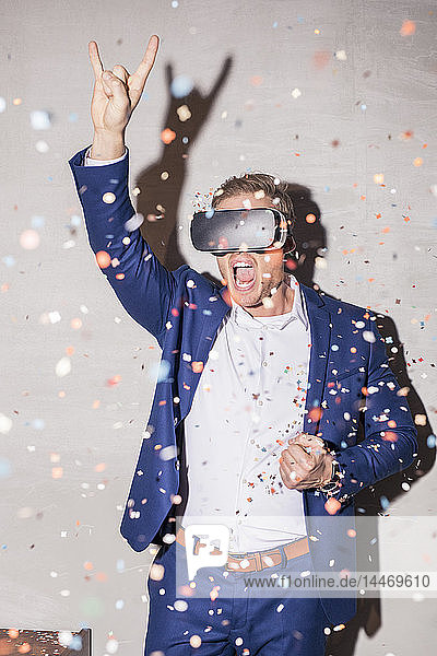Schreiender junger Mann mit Virtual-Reality-Brille steht zwischen Konfetti-Dusche auf einer Party