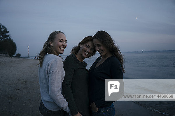 Deutschland  Hamburg  glückliche Mutter mit zwei Teenager-Mädchen abends am Strand am Elbufer