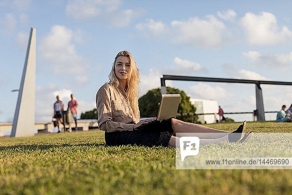 Young businesswoman sitting on a meadow using laptop