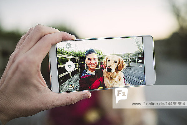 Handy-Bild einer glücklichen jungen Frau mit ihrem Golden-Retriever-Hund im Freien