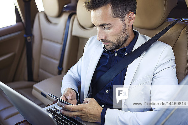 Young businessman working from the backseat of a car