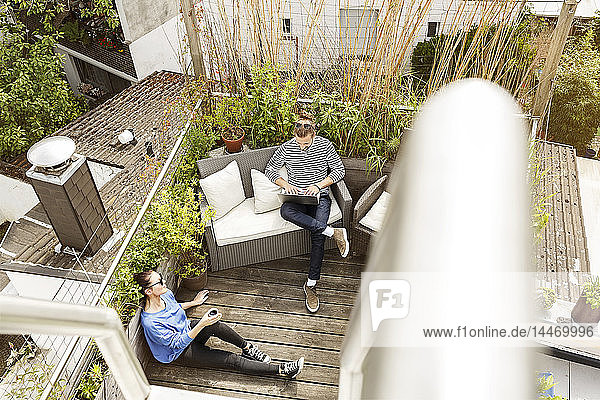Junges Paar entspannt sich auf dem Balkon  sitzt auf der Couch und benutzt einen Laptop