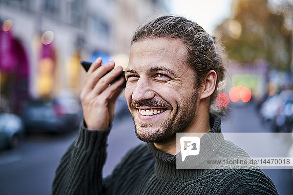 Portrait of laughing young man using smartphone on the street in the evening