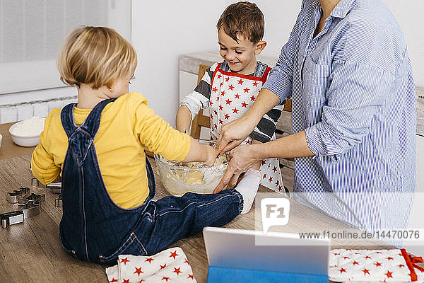 Boy preparing dough together with mother and little sister