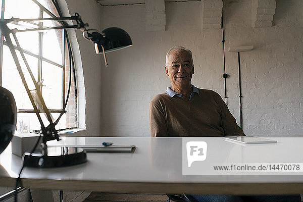 Porträt eines lächelnden älteren Geschäftsmannes am Schreibtisch sitzend im Büro