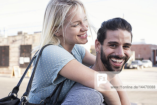 Glücklicher junger Mann trägt seine Freundin huckepack