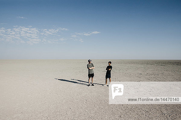 Zwei junge Männer stehen mit verschränkten Armen in der Wüste