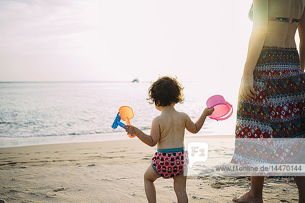 Thailand  Koh Lanta  Rückenansicht eines kleinen Mädchens mit Spielzeug am Strand bei Sonnenuntergang