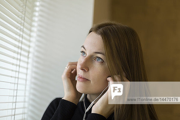 Portrait of woman near window putting on earphones