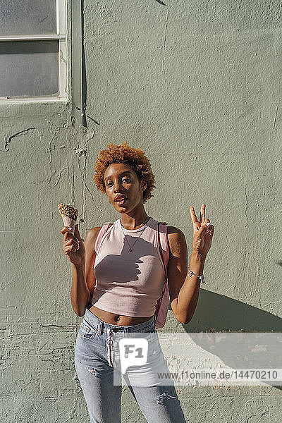 Portrait of young woman with ice cream cone posing at a wall