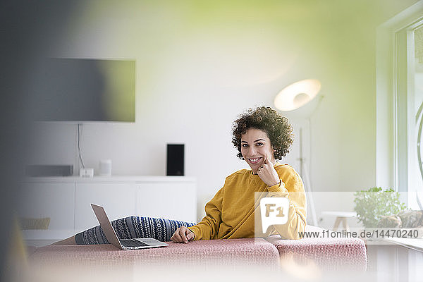 Lächelnde Frau mit Laptop auf der Couch zu Hause