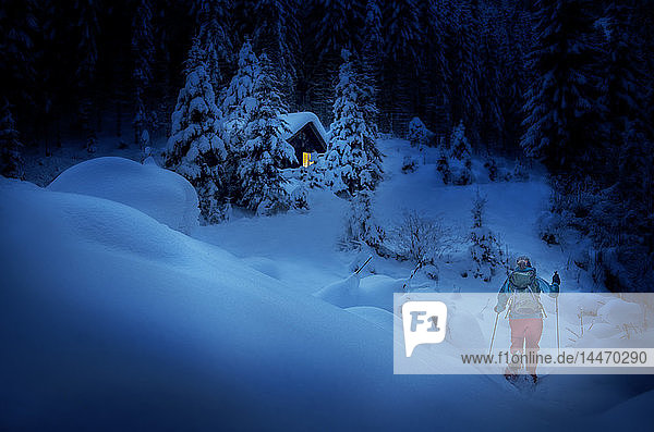 Österreich Bundesland Salzburg Schneeschuhwandern Frau nachts in der Nähe der Hütte
